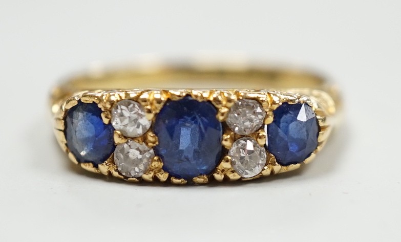A late Victorian 18ct gold and three stone sapphire set ring, with four stone diamond set spacers, size M, gross weight 4.1 grams.
